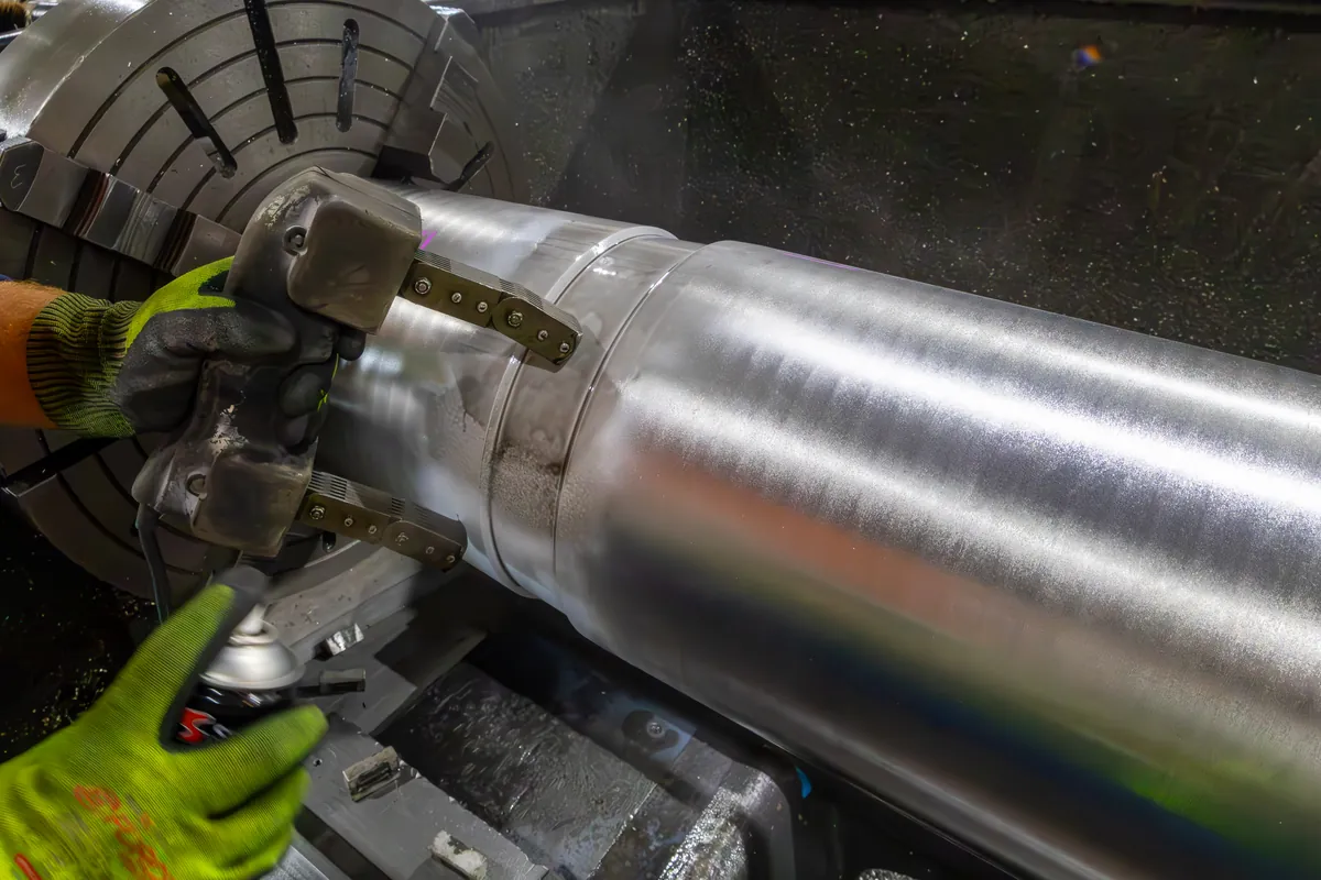 APEC technician crack testing a steel shaft with a magnetic particle yoke over white contrast paint