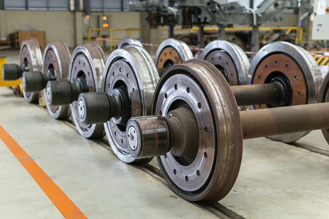 Row of large ferromagnetic railway wheelsets laid out on a factory floor, ready for magnetic particle inspection to detect surface and near-subsurface defects.