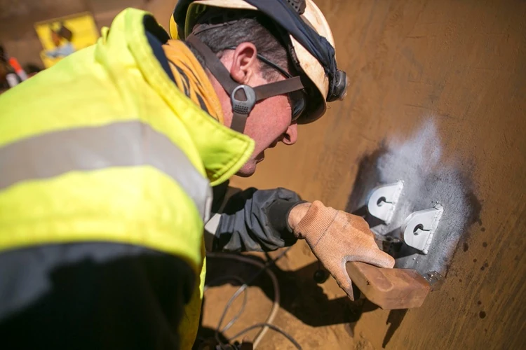 Male miner conducting Magnetic Particle Inspection on a one-ton crane lifting lug at a construction site in Perth, Australia, ensuring safety and material integrity