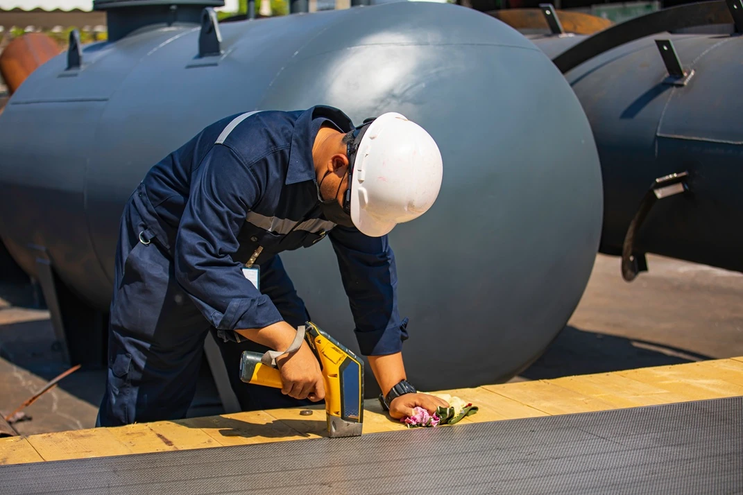 Technician wearing safety gear performing positive material identification testing on industrial equipment with handheld XRF analyser, inspected by APEC Inspection
