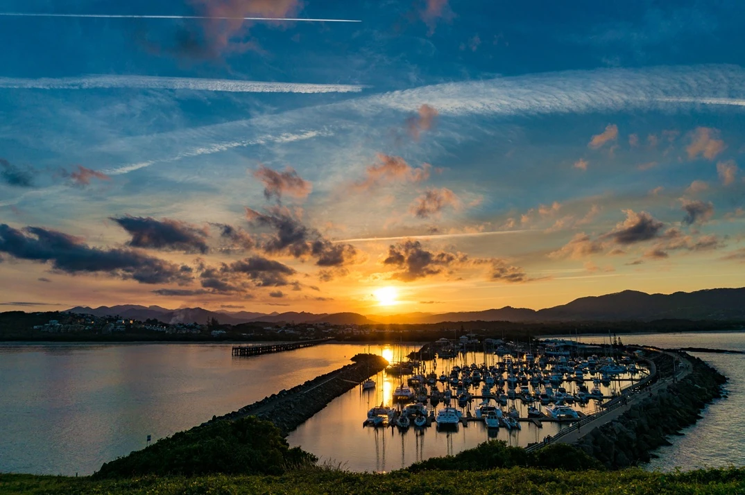 Sunset over Muttonbird Island Nature Reserve in Coffs Harbour, Australia, with dramatic clouds and visible plane trails in the sky.
